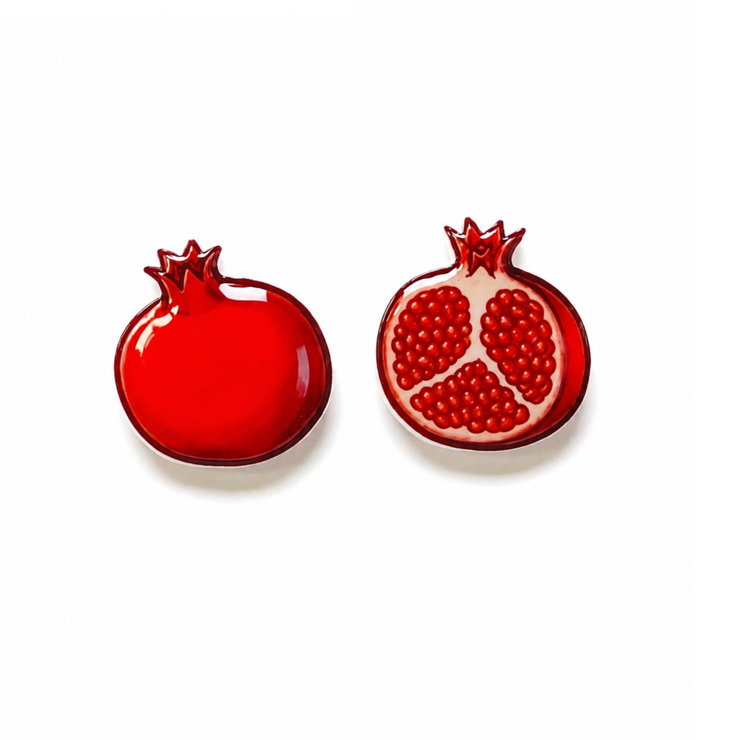 Two red pomegranate-shaped titanium stud earrings on a white background, one whole and one sliced open to show the seeds.