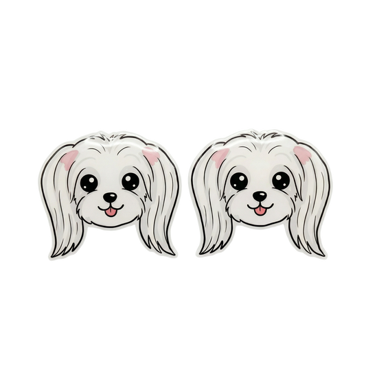 Two matching Maltese dog face accessories shown side by side on a plain white background. The design features a white fluffy dog head with black outlines, pink inner ears, and a small pink tongue sticking out.