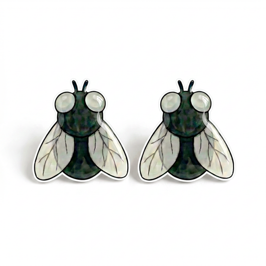 A pair of insect stud earrings shaped like flies, featuring a dark green textured body, large white eyes, and translucent white wings with black veining, set against a plain white background.